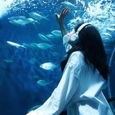 a woman wearing headphones standing in front of a large aquarium with fish swimming around