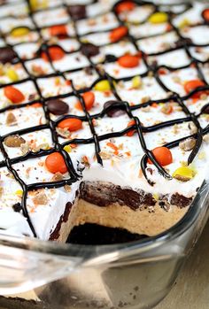 a cake with white frosting, chocolate and candy on top is in a glass dish