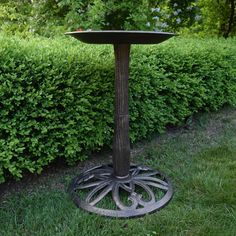 a bird bath sitting on top of a metal stand in the middle of some grass