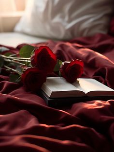 three red roses are laying on a bed next to an open book and some flowers