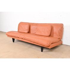 an orange leather couch sitting on top of a hard wood floor next to a white wall