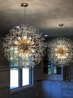 two chandeliers hanging from the ceiling in a room with windows and cupboards