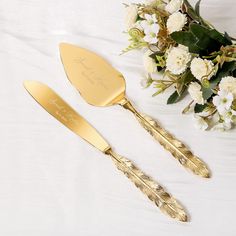 two gold colored utensils and a bouquet of flowers on a white tablecloth