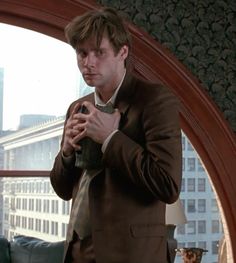 a man standing in front of a window looking at his cell phone while wearing a suit and tie