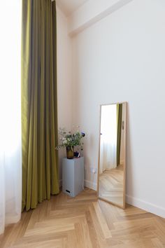 a mirror sitting on top of a hard wood floor next to a green drapes