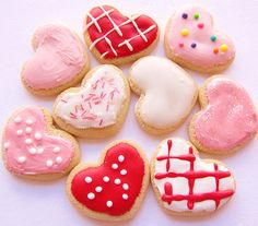 a bunch of cookies that are sitting on a white tablecloth with pink, red and white icing