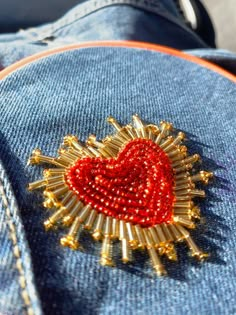 a red heart brooch sitting on top of a pair of blue jean pants with gold pins