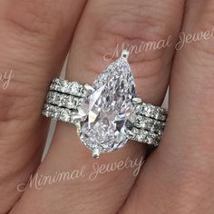 a woman's hand holding a ring with a pear shaped diamond on it and two rows of diamonds around the band