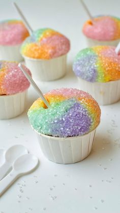 cupcakes with rainbow frosting and sprinkles on white surface next to utensils