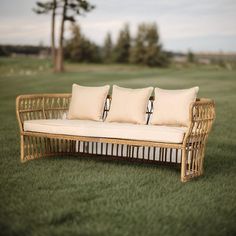 three pillows are placed on a wicker couch in the middle of a grassy field