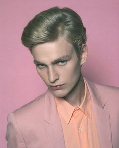 a man in a pink suit and orange shirt is looking at the camera with his eyes closed