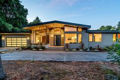 a modern home in the evening with lights shining on it's windows and doors