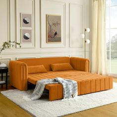 an orange couch sitting on top of a white rug in a living room next to a window