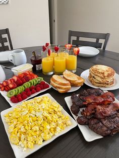 a table topped with plates of food and fruit next to eggs, bacon, pancakes