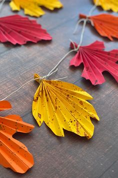 colorful paper leaves are hanging from strings on a table with string attached to the sides