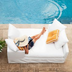 a man laying on top of a white couch next to a swimming pool with pillows