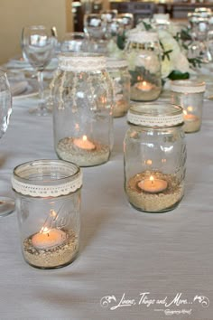 mason jars filled with sand and lit candles on top of a table covered in white flowers