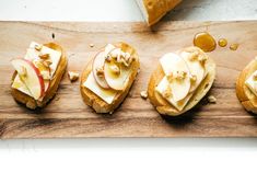 four pieces of bread with apples and cheese on them sitting on a wooden cutting board