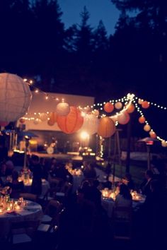 a group of people sitting around tables with lights on them and paper lanterns hanging from the ceiling