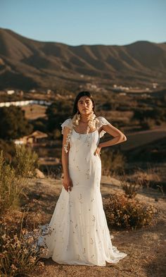 a woman in a wedding dress standing on a hill