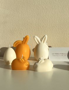 three small ceramic rabbits sitting next to each other on a white counter top with a business card in front of them