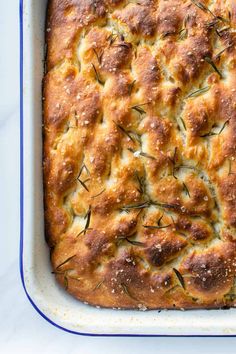 a square casserole dish filled with bread and topped with rosemary sprigs