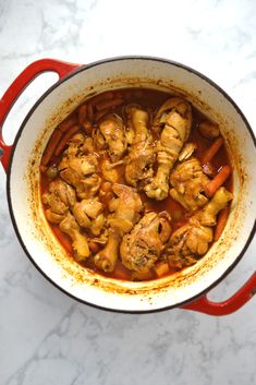 a pot filled with chicken and carrots on top of a white counter next to a spoon