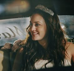 a woman sitting in the back seat of a car with a tiara on her head