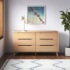 a room with a plant and a painting on the wall next to a wooden dresser