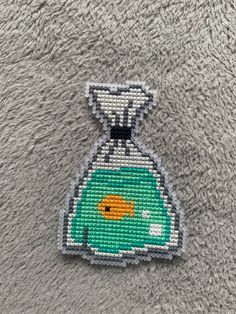 a needlepoint picture of a fish in a flask on a gray background,