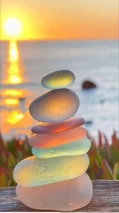 a stack of rocks sitting on top of a wooden table next to the ocean at sunset