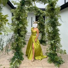 a woman in a yellow dress is walking through an archway with greenery on it