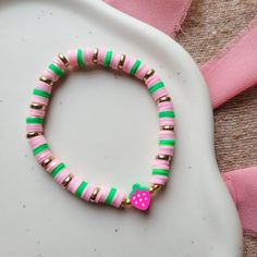 a pink and green beaded bracelet with a heart charm on it's end