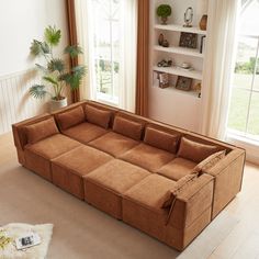 a living room with a large brown couch in the center and windows on both sides