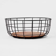 a black wire basket with a wooden cutting board in front of it on a white background