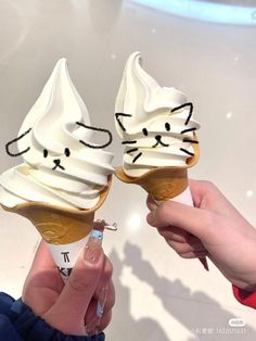 two ice cream cones with cats on them being held up by someone's hands