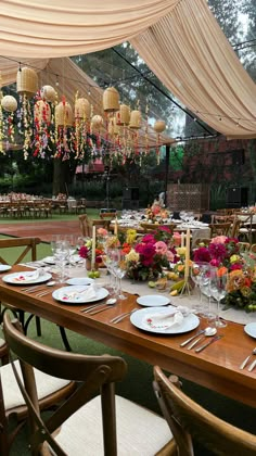 a table set with flowers and plates under a tented area for an outdoor event