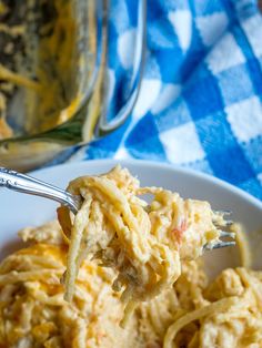 a fork full of spaghetti being lifted from a white plate with blue and white checkered table cloth