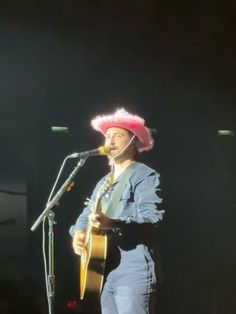 a man wearing a pink hat and holding a guitar in front of a microphone on stage