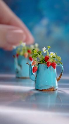 miniature teapots with strawberries and daisies on them are being held by a hand