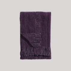 a purple blanket with fringes on it and a gray background in the foreground