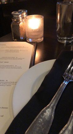 an empty plate and silverware sit on a table next to a menu with candles