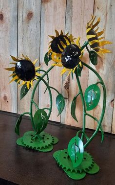 two metal sunflowers with green leaves are on a table