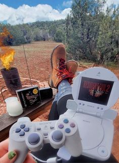 a person holding a video game controller in front of a fire pit with an open laptop on it