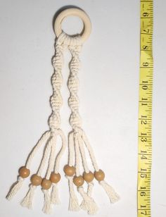 a white rope with wooden beads hanging from it's end next to a measuring tape