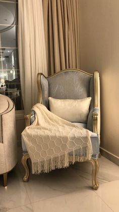 a chair sitting next to a window covered in curtains and a white blanket on top of it