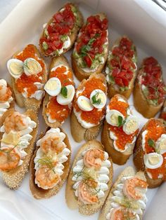 a white box filled with lots of different types of appetizers on top of bread