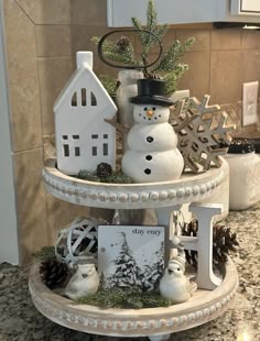 a three tiered tray with snowmen and houses on it's sides in a kitchen