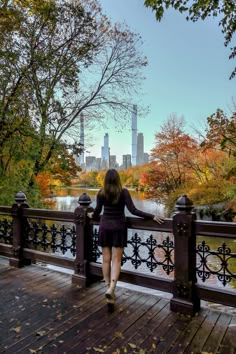 a woman standing on a bridge looking at the water and trees with fall foliage in the background