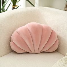 a pink pillow sitting on top of a white couch next to a potted plant